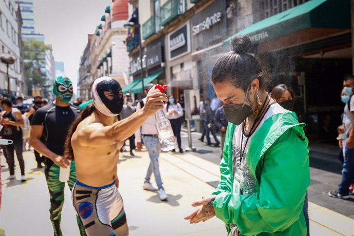 10 May 2021, Mexico, Mexico City: A peddler is being sanitized by a Mexican wrestler during an event at the streets of Mexico City called by the Mexican City Youth Institute to encourage the use of face masks amid the spread of the coronavirus pandemic.