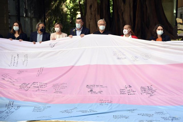 El president de les Corts Valencianes, Enric Morera (4i); el alcalde de Valencia, Joan Ribó (5i); y la vicepresidenta del Consell y consellera de Políticas Inclusivas, Mónica Oltra (d), sostienen la Bandera Trans tras una firma conjunta como muestra de ap