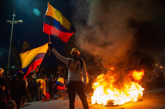 12 May 2021, Colombia, Bogota: A demonstrator waves a Colombian flag in front of burnt tires during a protest against the government of Colombian President Ivan Duque Marquez. Photo: Chepa Beltran/LongVisual via ZUMA Wire/dpa