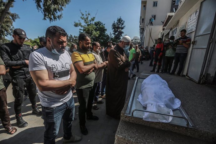 15 May 2021, Palestinian Territories, Gaza City: Palestinians pray outside the morgue of Al-Shifa Hospital near the body of a Palestinian who was killed after an Israeli airstrike. Eight children and two women from the Abu Hatab family were killed after