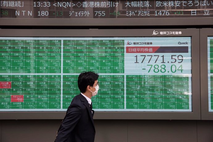 Archivo - 13 March 2020, Japan, Tokyo: A man wearing a surgical mask as a protective measure against coronavirus infection walks past an electronic board showing the numbers for the Nikkei 225 index on the Tokyo Stock Exchange. Photo: Stanislav Kogiku/S