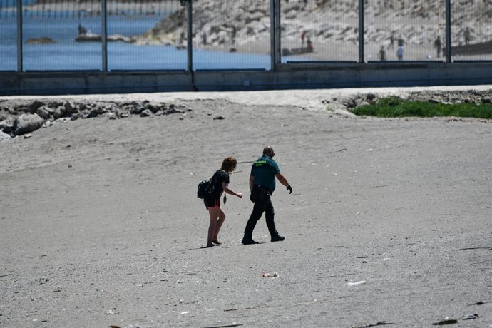 Un agente de Guardia Civil con un joven migrante marroquí sale de una playa de Ceuta