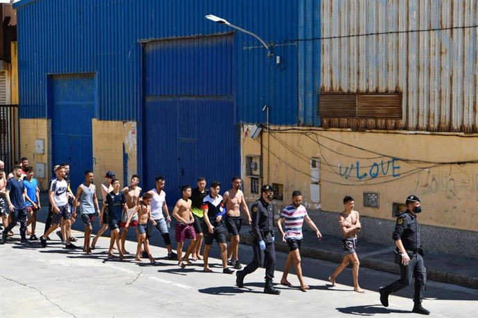 Un grupo de jóvenes migrantes marroquíes en fila en las inmediaciones de una nave de Ceuta tras acceder a la ciudad española 