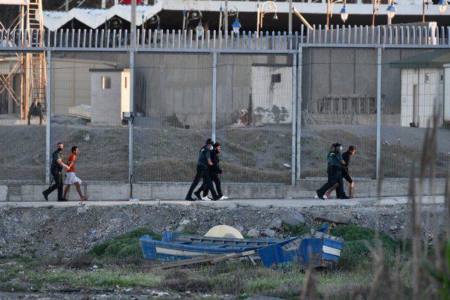 Agentes de Policía y personas migrantes en la playa del Tarajal, a 17 de mayo de 2021, en Ceuta (España). España ha movilizado al Ejército en la ciudad tras la entrada de más de 5.000 marroquíes en 24 horas.