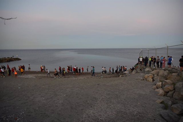 Personas migrantes caminan por la playa del Tarajal tras acceder a Ceuta de forma irregular
