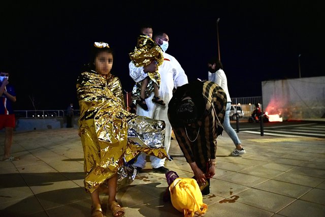 Un hombre migrante coge en brazos a un menor acompañado de una mujer y una niña pequeña, a 17 de mayo de 2021, en Ceuta (España). España ha movilizado al Ejército en la ciudad tras la entrada de más de 5.000 marroquíes en 24 horas.