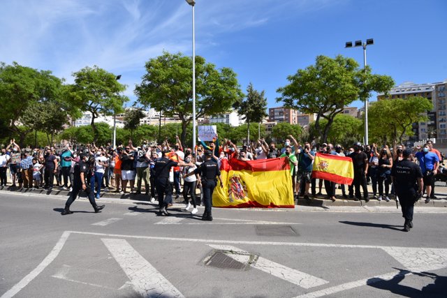Varias personas se concentran con carteles y banderas de España frente al coche del presidente del Gobierno y el ministro de Interior , a su llegada al Helipuerto de Ceuta, a 18 de mayo de 2021, en Ceuta (España)