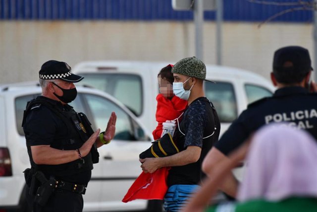 Un policía junto a hombre migrante que coge en brazos a una niña en la playa del Tarajal, a 17 de mayo de 2021, en Ceuta (España). España ha movilizado al Ejército en la ciudad tras la entrada de más de 5.000 marroquíes en 24 horas.