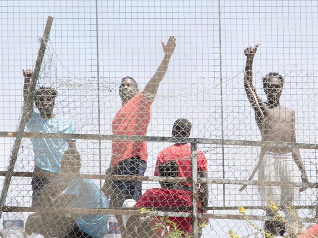 Varios migrantes detrás de una valla en la Ciudad del Fútbol del Altos del Real a 18 de mayo de 2021, en Melilla (España). Un total de 86 de migrantes de origen subsahariano --85 hombres y una mujer-- han entrado este martes en Melilla bordeando el dique 