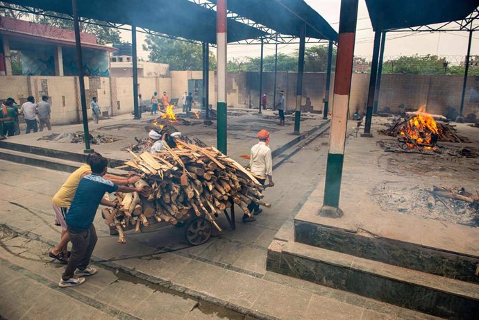 Transporte de madera para la incineración de muertos por coronavirus en un crematorio en India