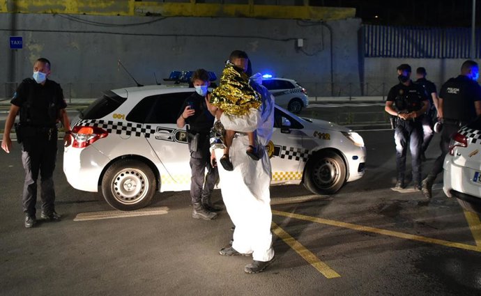 Un hombre migrante coge en brazos a un menor, en la primera noche de llegada de inmigrantes a Ceuta, el pasado día 17 de mayo