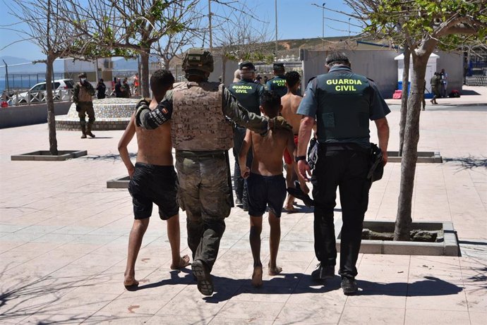 Un militar del ejército español y un agente de la Guardia Civil ayudan a dos menores migrantes procedentes de Marruecos a su llegada a Ceuta