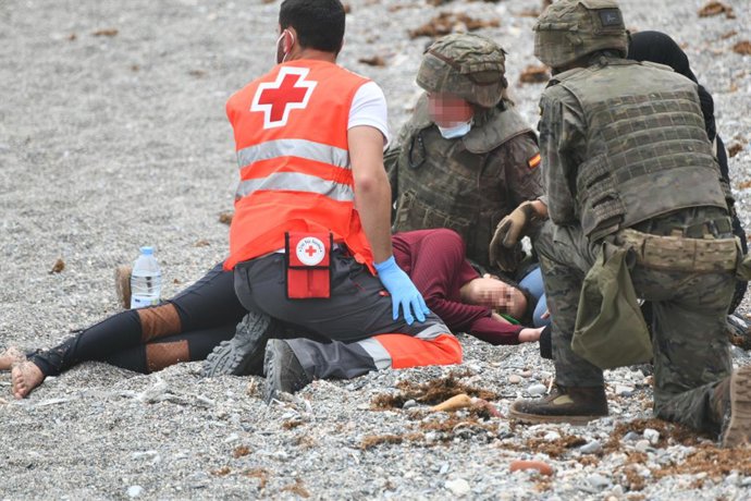 Un trabajador de la Cruz Roja y dos militares ayudan a una migrante que ha llegado a la orilla en una jornada marcada por las devoluciones en caliente que están efectuando a los migrantes que han entrado en Ceuta procedente de Marruecos, a 18 de mayo de
