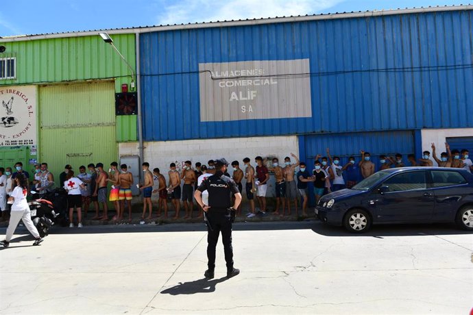 Un grupo de jóvenes migrantes marroquíes en fila en las inmediaciones de una nave en Ceuta tras acceder de forma irregular a la ciudad española