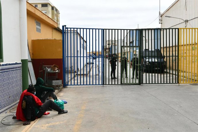 Dos subsaharianos esperan para ser atendidos en la puerta de las naves del Tarajal en Ceuta