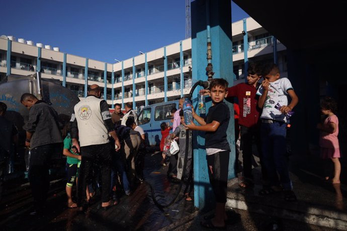 Unos niños se reúnen junto a un camión de agua para llenar botellas de agua potable.