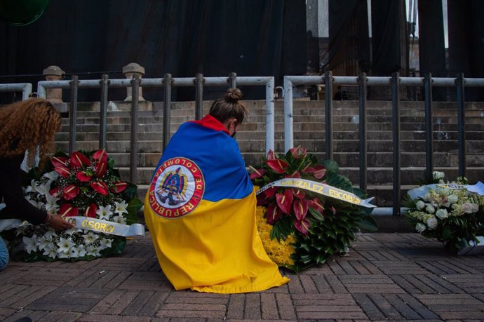 24 May 2021, Colombia, Bogota: A demonstrator wearing a Colombian flag sets a funeral wreath at the entrance of Colombian Congress as citizens and demonstrators support the congress session in which Minister of Defense Diego Molano was put into Motion o