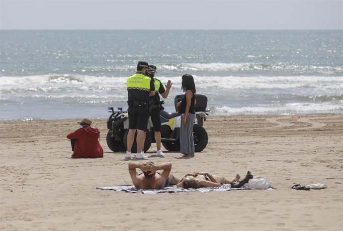 Dos policías municipales hablan con una mujer en una playa de Valncia, a 26 de mayo de 2021. 