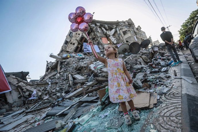 25 May 2021, Palestinian Territories, Gaza City: A girl holds balloons near the Hanadi Tower in the middle of Al-Rimal Market, one of the buildings damaged in Israeli air strikes. Photo: Mohammed Talatene/dpa