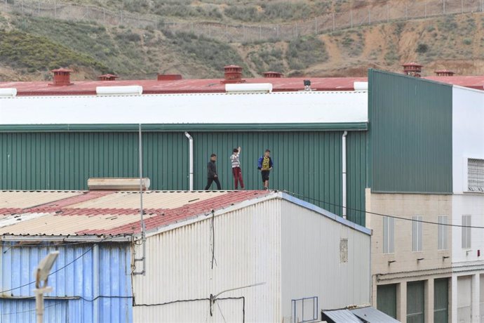 Varios niños caminan por un tejado al tratar de escapar de la nave de primera acogida del polígono del Tarajal, en Ceuta.