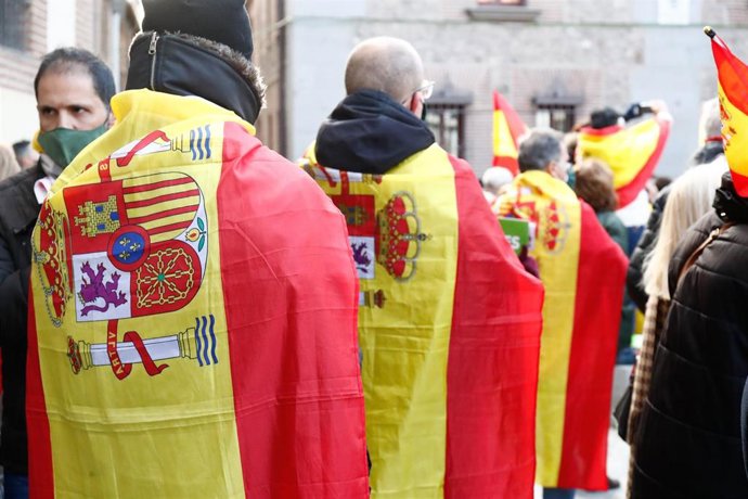 Archivo - Varias personas se cubren con banderas de España durante una concentración de Vox en defensa de la Constitución y contra el Gobierno de Pedro Sánchez, en la Plaza de la Villa, en Madrid (España), a 6 de diciembre de 2020. La formación liderada