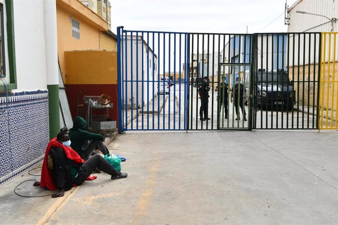 Dos subsaharianos esperan para ser atendidos en la puerta de las naves del Tarajal, en Ceuta.