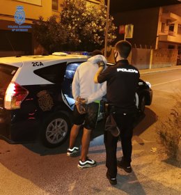 Un agente de la Policía Nacional acompaña a uno de los detenidos al coche patrulla.