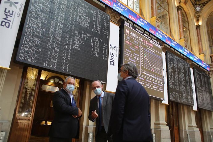Tres hombres observan valores económicos en el Palacio de la Bolsa.