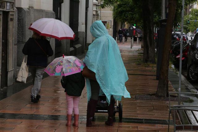 Archivo - Una mujer y una niña pasean con paraguas en la capital en un día de lluvia. Archivo.