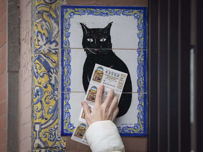Archivo - Una persona pasa varios  décimos de lotería de Navidad por el azulejo de la administración 'El gato negro'. En Sevilla (Andalucía, España), a 18 de diciembre de 2020.