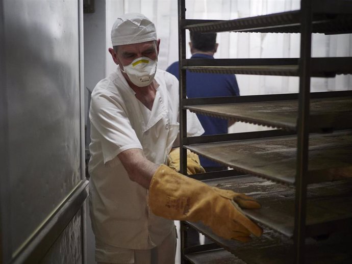 Archivo - Un trabajador protegido con mascarilla maneja bandejas para cocer pan.