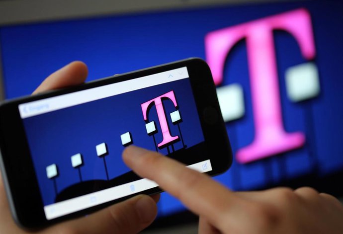 Archivo - Una mujer mira en su móvil el logo de Deutsche Telekom