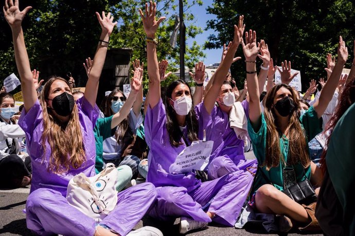 25 May 2021, Spain, Madrid: Young medical students sitting on the ground raise their hands during the Resident Internal Doctors (MIR) demonstration in front of the Spanish Ministry of Health, to show their rejection of the new requirements for the choic