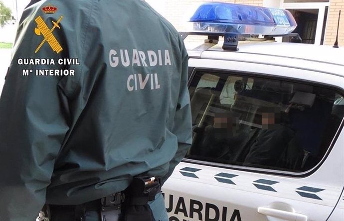 Archivo - Un agente de la Guardia Civil junto a un coche patrulla