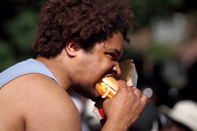 Archivo - Hombre comiendo una hamburguesa en la calle.