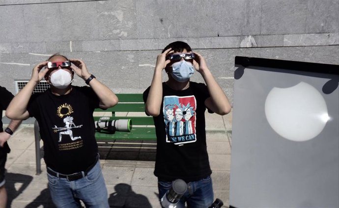 Dos personas contemplan en el exterior del planetario de Pamplona el eclipse solar parcial que se puede apreciar también proyectado en una superficie blanca, a 10 de junio de 2021.