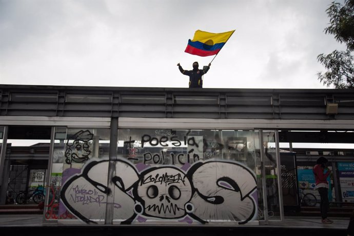 28 May 2021, Colombia, Bogota: A demonstrator waves a Colombian flag over a transmilenio bus stop that reads "S.O.S Colombia" during a protest against the government of President Ivan Duque Marquez. Colombian President Ivan Duque on Friday night said mi