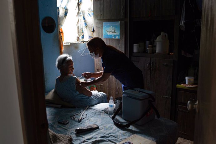 11 June 2021, Venezuela, Caracas: A health worker administers the first dose of the Corona vaccine Sputnik V to 74-year-old Ana Ortiz at her home. Photo: Pedro Rances Mattey/dpa