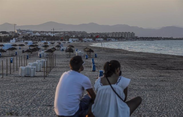 Archivo - Dos jóvenes sentados contemplan la playa de la Malvarrosa en València