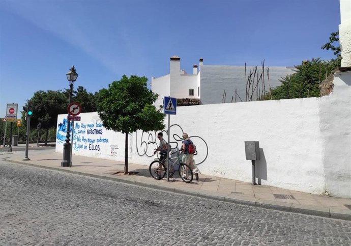 Dos turistas pasan junto al muro que delimita la parcela donde se proyecta el centro de ocio de la Cruz del Rastro.