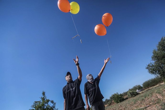15 June 2021, Palestinian Territories, Gaza City: Masked Palestinians release refrigerant gas-filled balloons, attached to incendiary devices and flammable material, to be propelled by wind into Israeli territory, from an area located to the east of Gaz