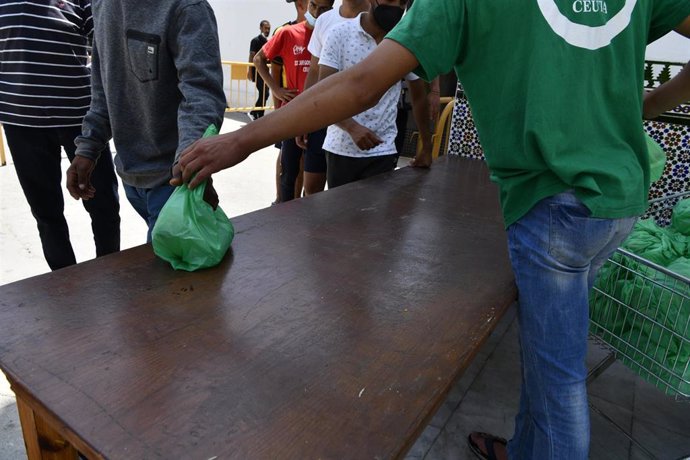 Un miembro de la asociación islámica 'Luna Blanca' reparte una bolsa de comida a varios migrantes en Ceuta (España), en una imagen de la pasada semana