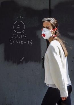 Archivo - Una chica con mascarilla pasa junto a una pintada relacionada con el COVID-19 durante el día 25 del estado de alarma decretado a consecuencia de la crisis del coronavirus, en Valencia (Comunidad Valenciana, España), a 8 de abril de 2020.