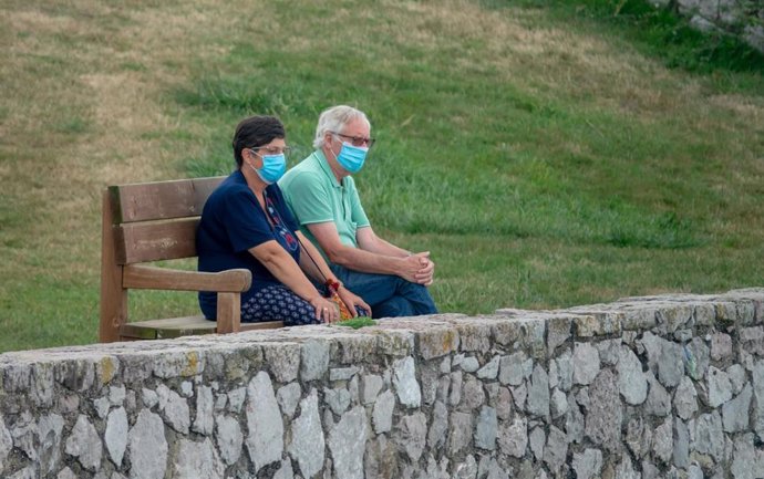 Archivo - Una pareja sentada con mascarillas en el denominado "el banco más bonito del mudo" en LLanes,  durante el verano de la pandemia Covid-19. Asturias a 25 de agosto del 2020