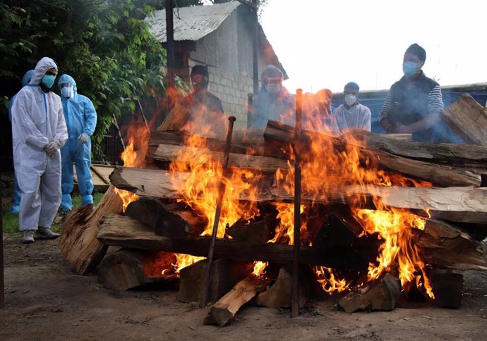 Familiares y allegados con trajes de protección junto a la pira funeraria de una víctima de COVID-19 en un crematorio de Srinagar. 