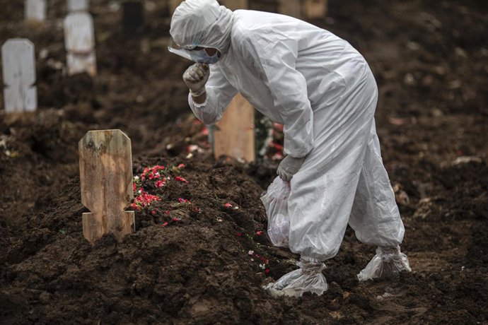 Archivo - 25 February 2021, Indonesia, South Jakarta: A COVID-19 virus victim family member in a protective suit mourns at the grave after the burial at a cemetery specifically for COVID-19 deaths. Photo: Donal Husni/ZUMA Wire/dpa