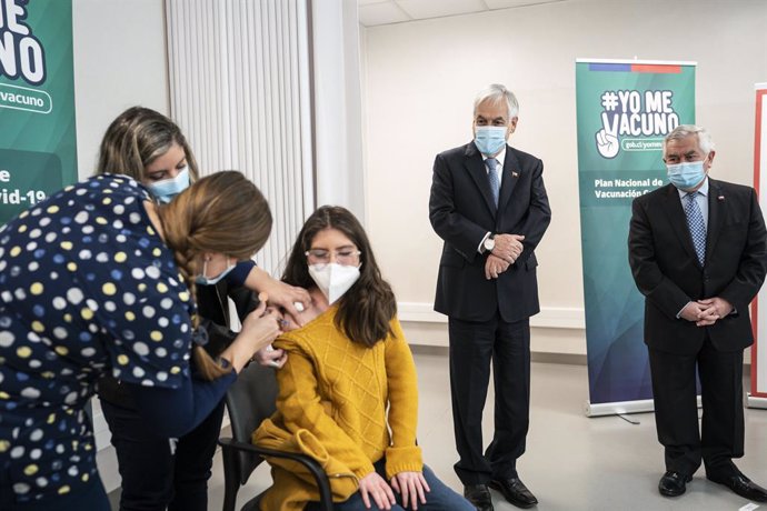 HANDOUT - 22 June 2021, Chile, Santiago: Chilean President Sebastian Pinera (2nd R) and Health Minister Enrique Paris (R) watch as a teenager receives a dose of Coronavirus vaccine, during the launch of the immunization campaign for youth under 18. Phot