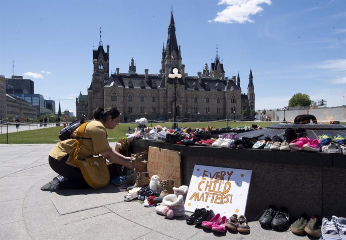 31 May 2021, Canada, Ottawa: An indigenous kneels in front of shoes placed on the Centennial Flame to honour more than 200 children whose remains have been found buried at a former residential school in Kamloops. Photo: Adrian Wyld/The Canadian Press vi