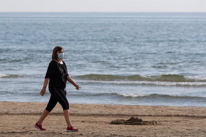 Archivo - Una mujer con mascarilla pasea por la playa de la Malvarrosa