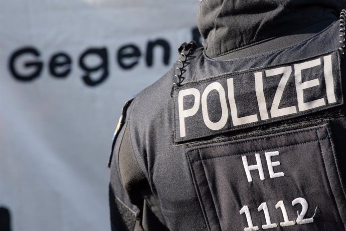 11 June 2021, Hessen, Frankfurt_Main: Thw word "Against" is written in German on a poster held by demonstrators, next to a policeman during a demonstration by left-wing alliances against right-wing structures in the police, following the disbandment of 